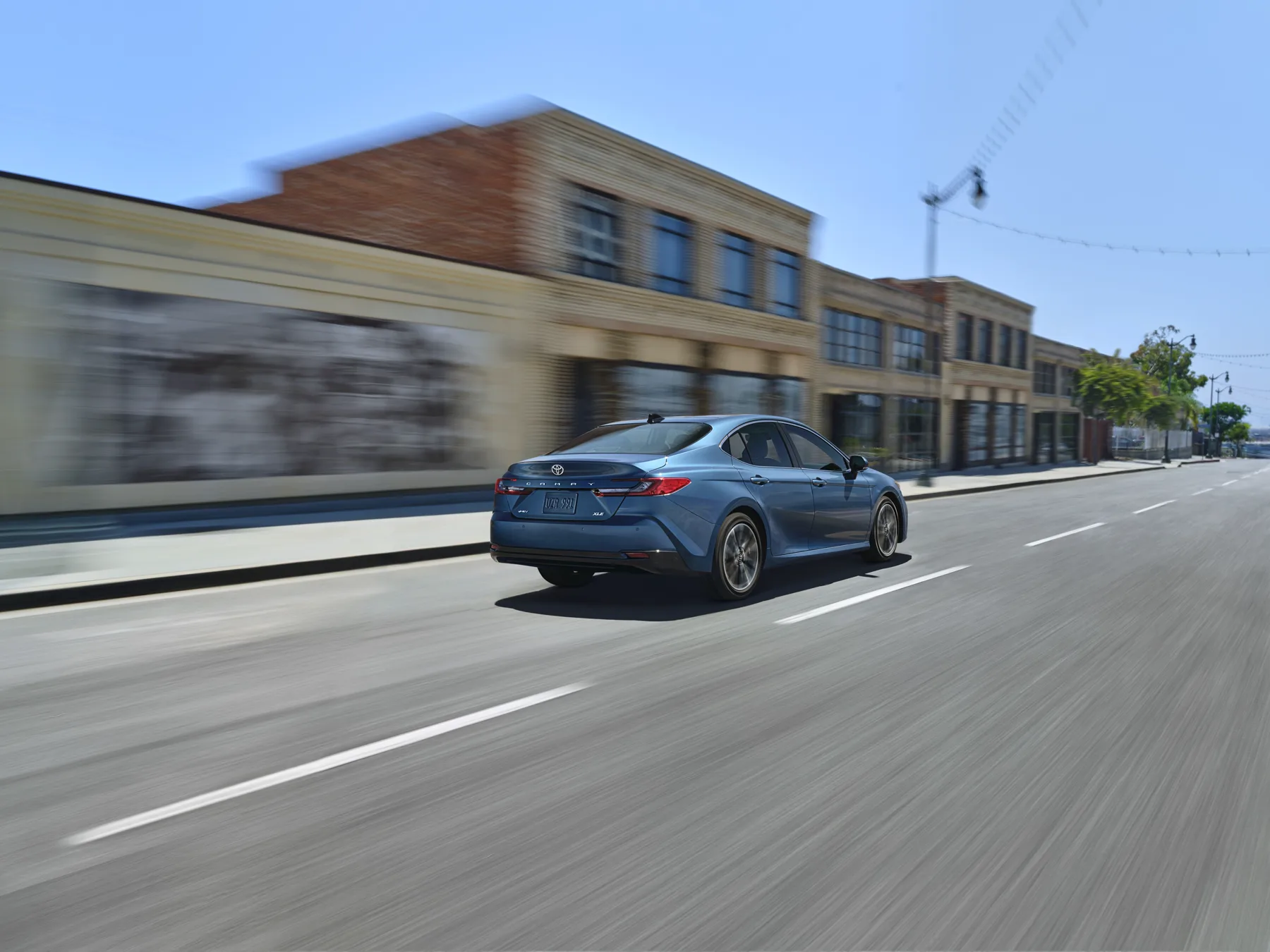 Blue 2025 Toyota Camry, rear three-quarter view in motion