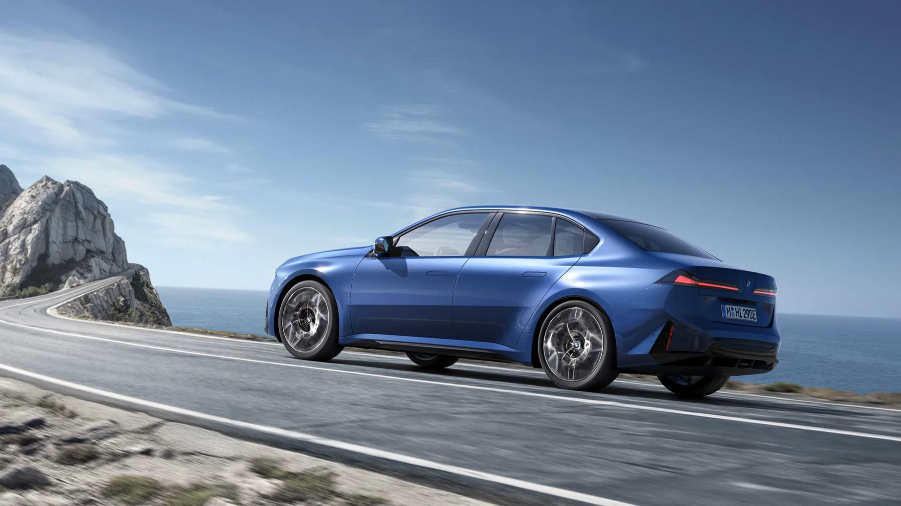 Blue 2026 BMW i3 50 xDrive, rear three-quarter on a coastal cliff road