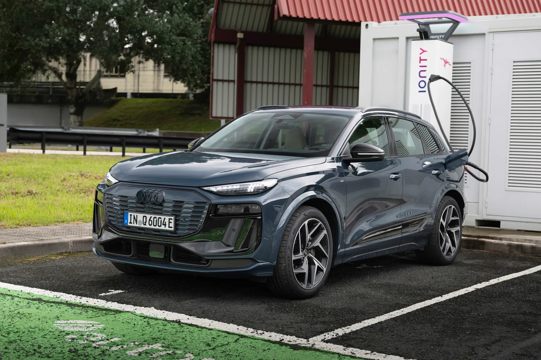 Dark 2026 Audi Q6 e-tron at a charger with the rear-flank charge door open