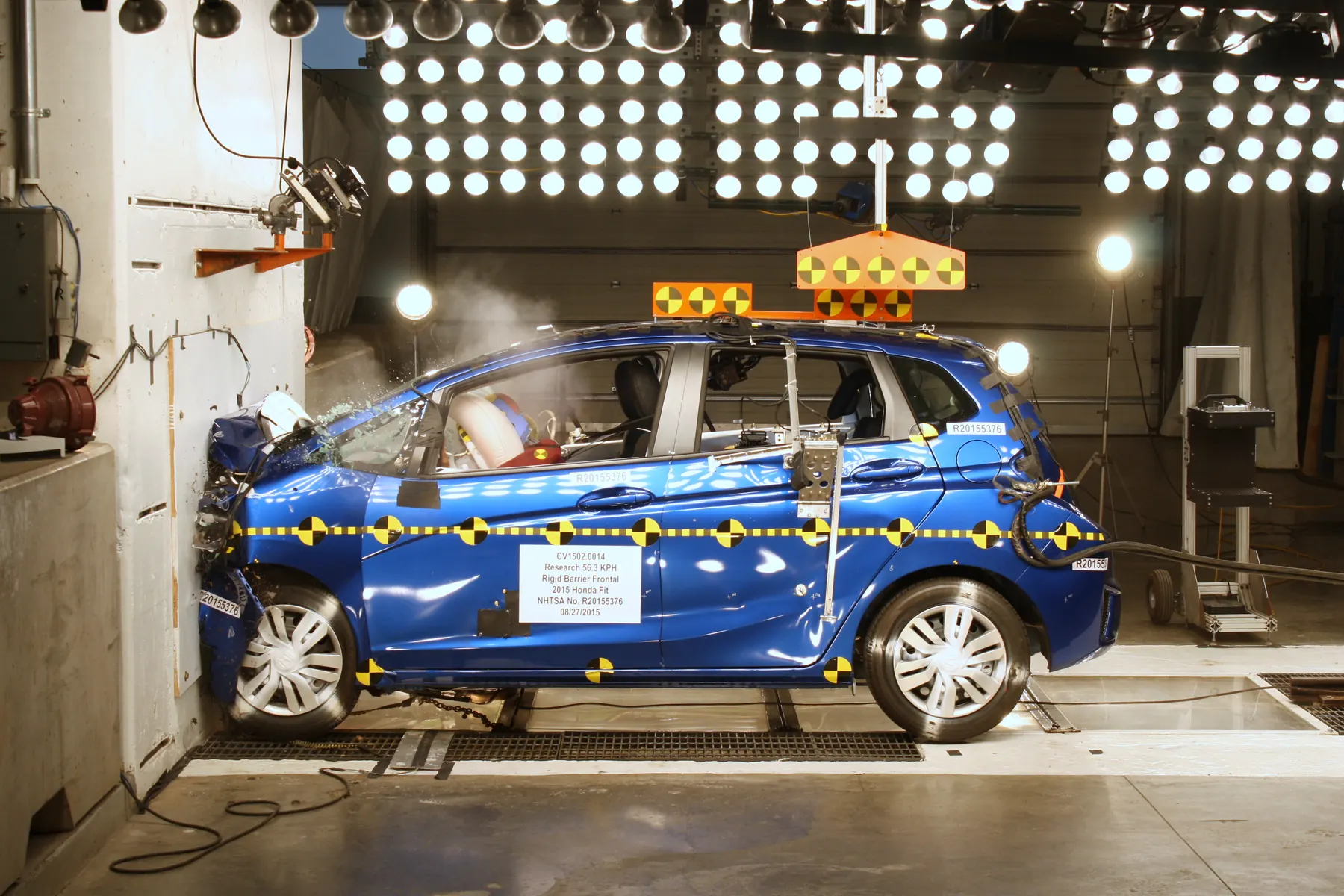 Blue Honda Fit in an official NHTSA rigid-barrier frontal crash test, nose crumpled against the wall